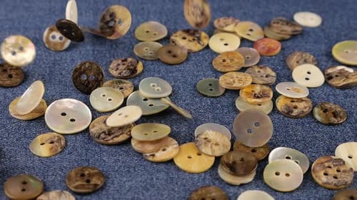 Natural mother of pearl buttons fall on denim. Slow motion.
