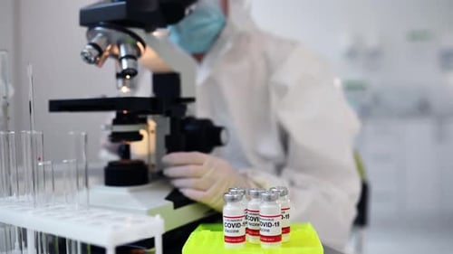 Clinic worker in safety uniform is in the lab with test tubes of COVID-19 vaccine