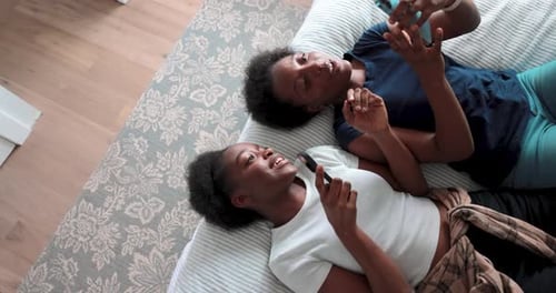 Two Women Laying on Bed Looking at Phones