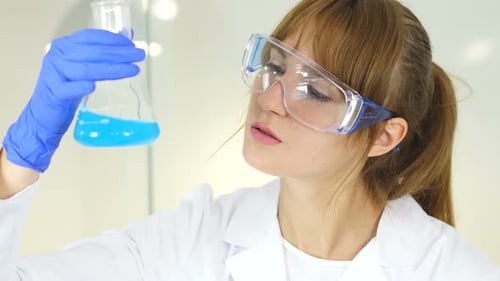 Woman Scientist Inspecting Blue Liquid in Lab Beaker