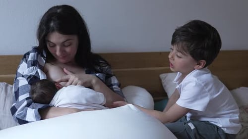 Mother Breastfeeding Infant with Child Nearby in Home