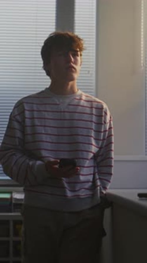 Jeune homme en pull rayé se tient près de la fenêtre lumineuse de la salle de conférence