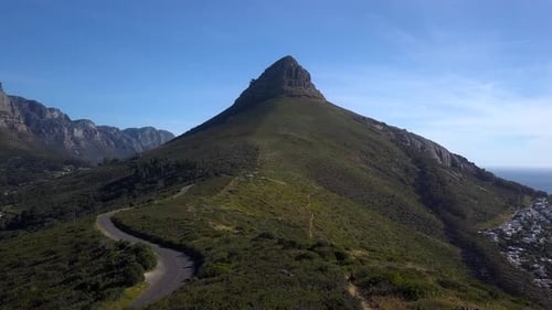 Drone follows an Empty windy road leading to the pointy Apex of Lions Head mountain, Sea Point, SA,