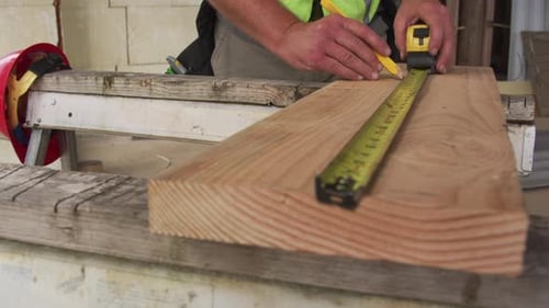 Construction Worker Measuring and Marking Lumber Board