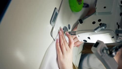 Vertical Video Close Up in the Sewing Workshop Young Girl Works with a Sewing Machine and White