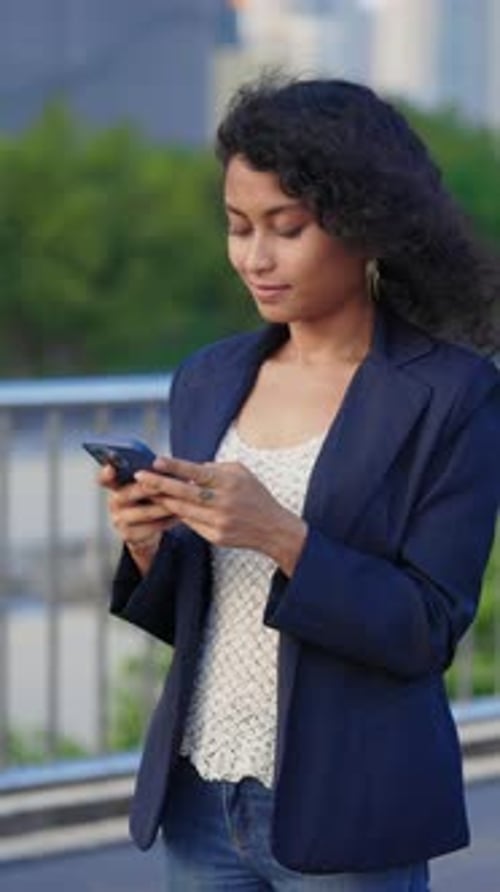 Vertical Video Smiling CurlyHaired Girl Standing on the Street And Responding To Messages on Mobile