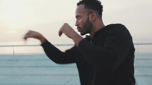 Young athlete boxer practicing punching technique while standing on the embankment