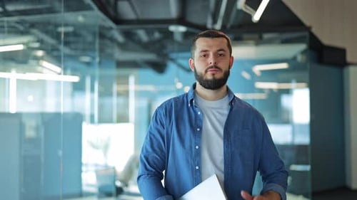 Confident Professional Man Smiles Holding Laptop in Modern Office