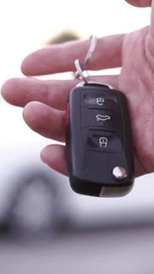 Nahaufnahme einer Person mit einem schwarzen Autofernschlüsselanhänger, die sich darauf vorbereitet, ein Fahrzeug zu entriegeln
