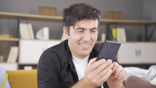 Man Smiling and Using Smartphone at Home