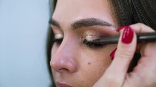 Closeup view of female hands applying eyeliner on young attractive woman's eyelids