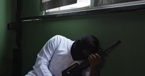 Man Crouching and Aiming a Rifle Indoors