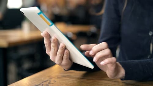 Woman Browsing Internet on Tablet Computer Sitting by Table in Cafe 30s