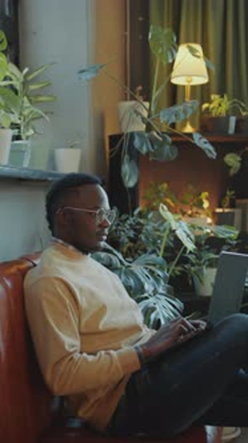 Young African American Man Working on Laptop on Couch in Office