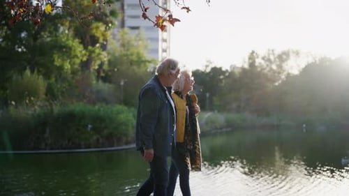 Feliz pareja mayor caminando por el lago en un parque urbano
