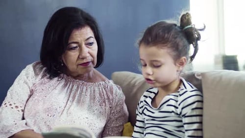 Grandmother and Granddaughter Reading a Book on Sofa
