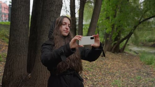 Woman Captures Fall Scenery Young Woman with Long Hair in Park During Autumn Walk Relaxed Influencer