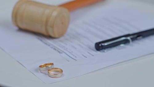 Two gold wedding rings on divorce decree papers with a wooden judge gavel and pen