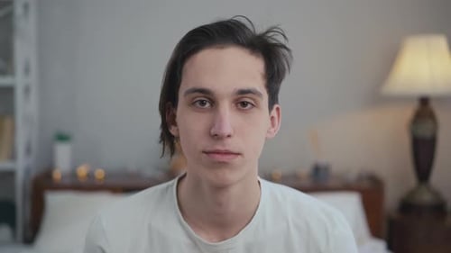 Closeup Portrait of Carefree Young Man Looking at Camera As Pillow Hitting Face in Slow Motion Front