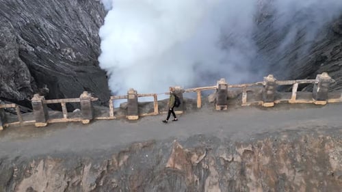 Woman Walking Along the Rim of Steaming Mount Bromo Volcano Crater in Indonesia
