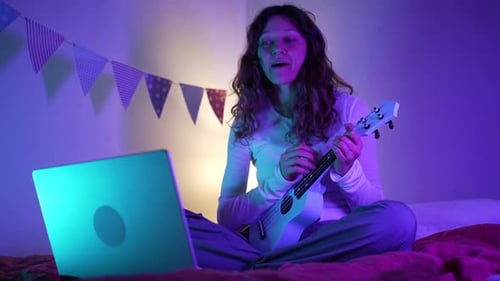 Woman Playing Ukulele and Talking to Laptop