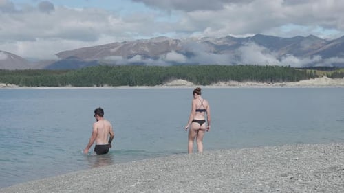 Young caucasian couple swimming in a cold blue lake in between forest and mountains on a sunny summe