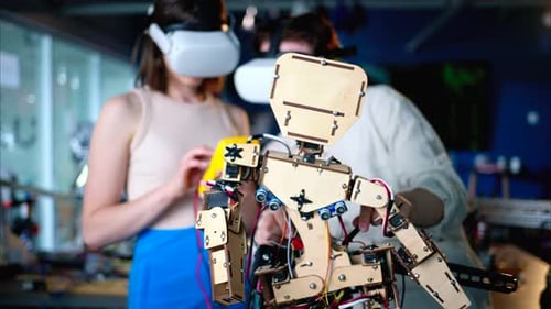 Two young engineers fixing a mechanical robot in the workshop, using VR virtual reality headsets