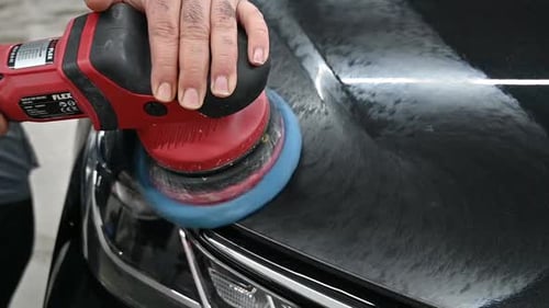Hands of repair man polishing modern black vehicle with industrial tool, close up view