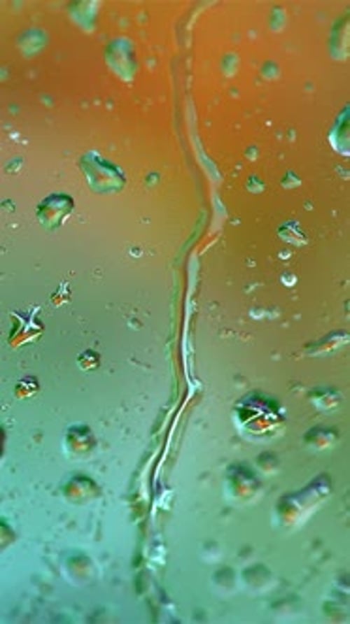 Raindrops on blur colorful background. Large drops flowing on glass window slowly in rainy weather.