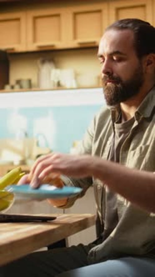 Vertical Video Remote Worker Eating Croissants and Using Laptop in a Kitchen Interior