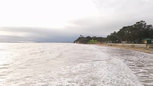 Low aerial flight above waves crashing on Narrow Neck beach