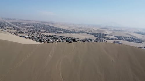 A pair of intrepid travelers stand on a dune near a town in the desert. Huacachina, Peru