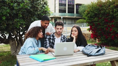 Collaborative multi-ethnic students working on laptop at campus outdoor