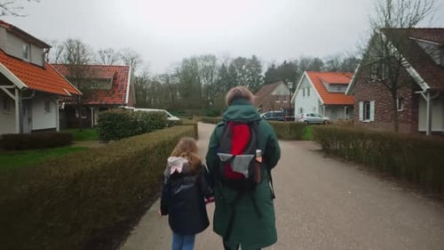 Mother and child with backpack and raincoat walking through bungalow village