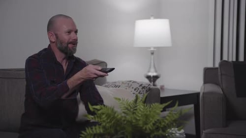 Man Watches Television, Changes Channels with Remote