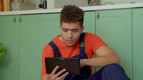 Man Uses Tablet in Kitchen Wearing Overalls