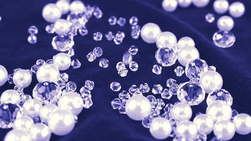 White pearls, clear jewelry crystals and rock crystal fall on blue velvet. Slow motion.