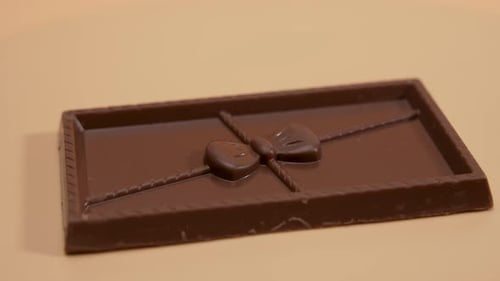 A chocolate bar with a bow rotates on an orange background.