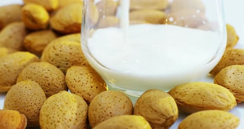 The almond milk is poured into a glass in slow motion, the background in woods there are almonds,