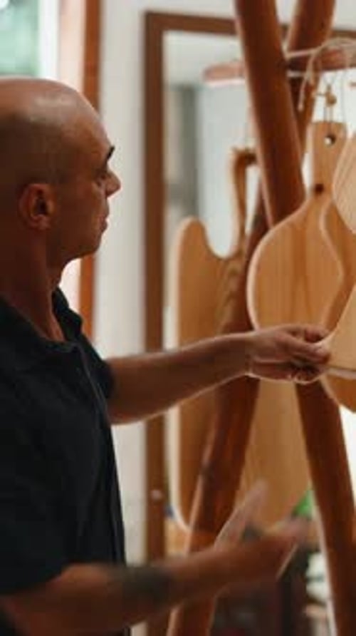 Male Artisan and Luthier Inspecting the Quality of a New Guitar Body in His Workshop