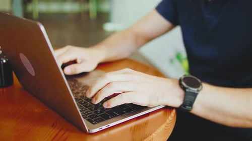 Man Typing on Laptop Keyboard at Wooden Table