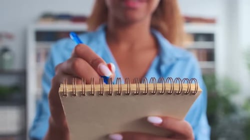 Nahaufnahme einer afroamerikanischen Frau mit Stift, die Notizen im Notizblock macht