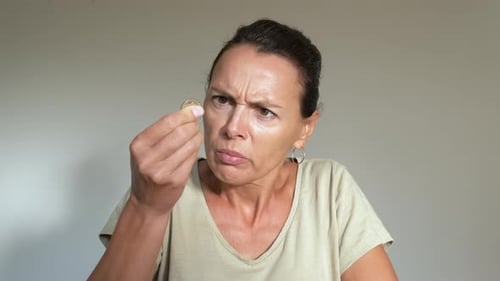 Woman Examining Coin with Concerned Expression Indoors