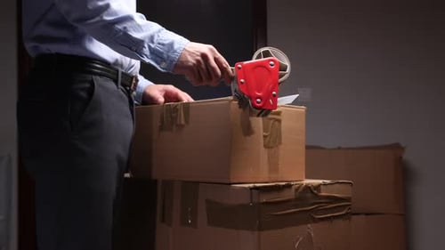 Man sealing cardboard box with tape gun in home