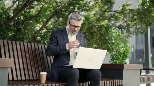 Adult Using Laptop on Park Bench Blows Nose