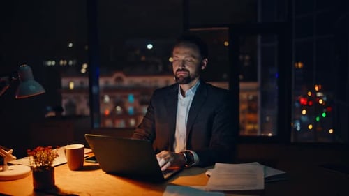 Homme concentré travaillant sur un ordinateur portable, appartement panoramique de nuit, gros plan, employé satisfait
