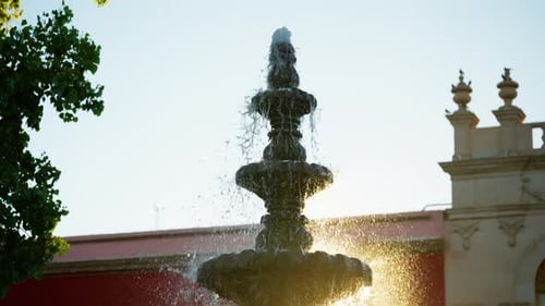 Ornate Stone Fountain Spraying Water with Golden Sunlight and Historic Building