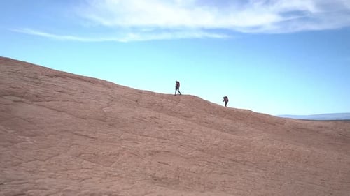 Couple of Hikers Walking on Rocky Sandstone Hill With Desert Patterns Under Blue Sky, Full Frame Slo