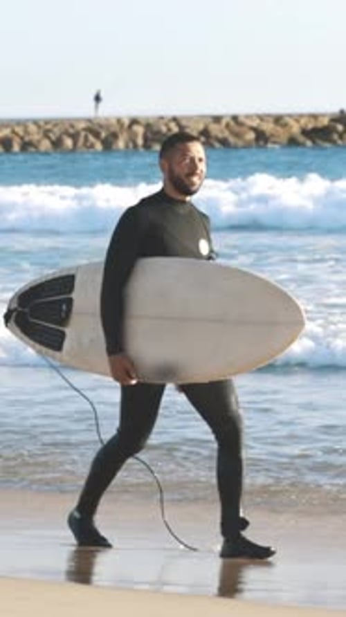 Man Carries Surfboard on Beach, Ocean Waves Background
