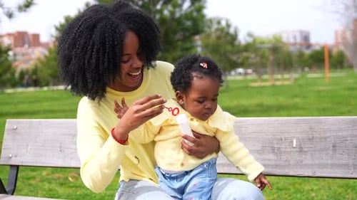 African Woman and Daughter Playing with Soap Bubbles in a Park